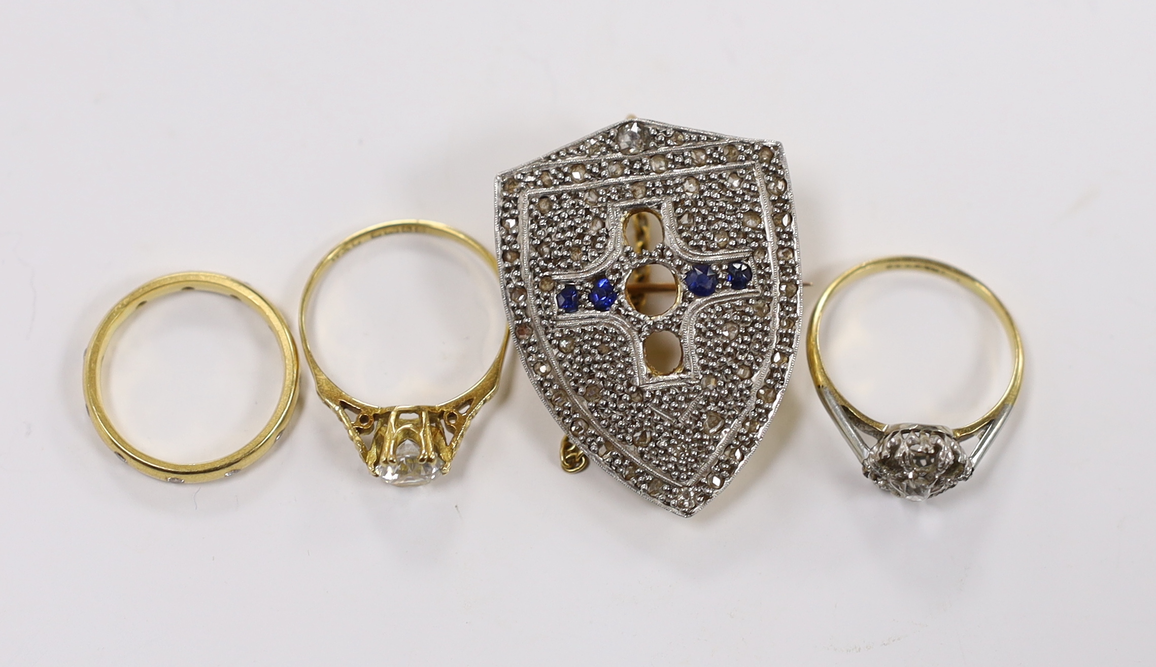 A late 19th century yellow metal, rose cut diamond and sapphire cluster set shield shaped brooch (three stones missing), 35mm and three rings including modern 18ct gold and gypsy set eternity, an 18ct and single stone di